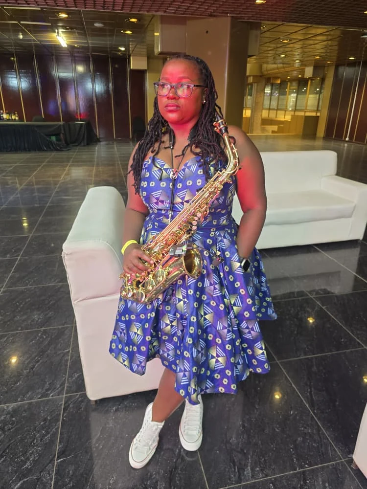 Tina Watyoka with saxophone in a blue patterned dress
