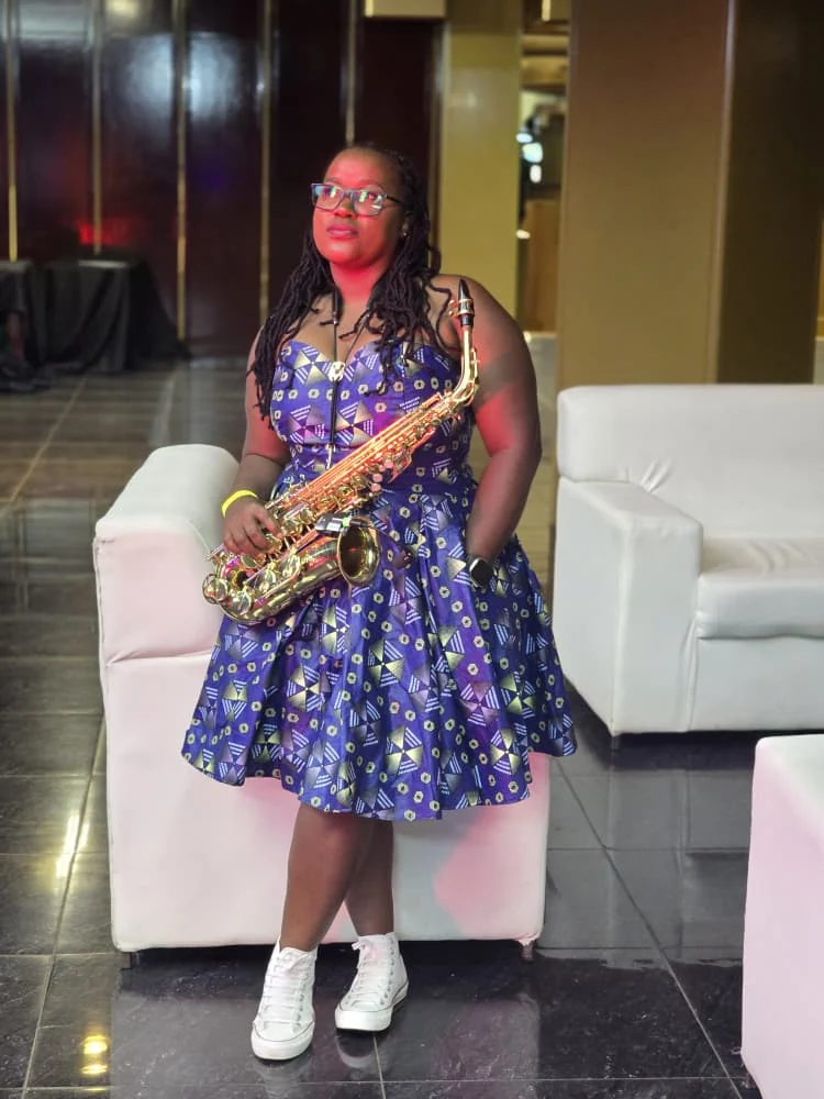 Tina Watyoka with saxophone in a blue patterned dress