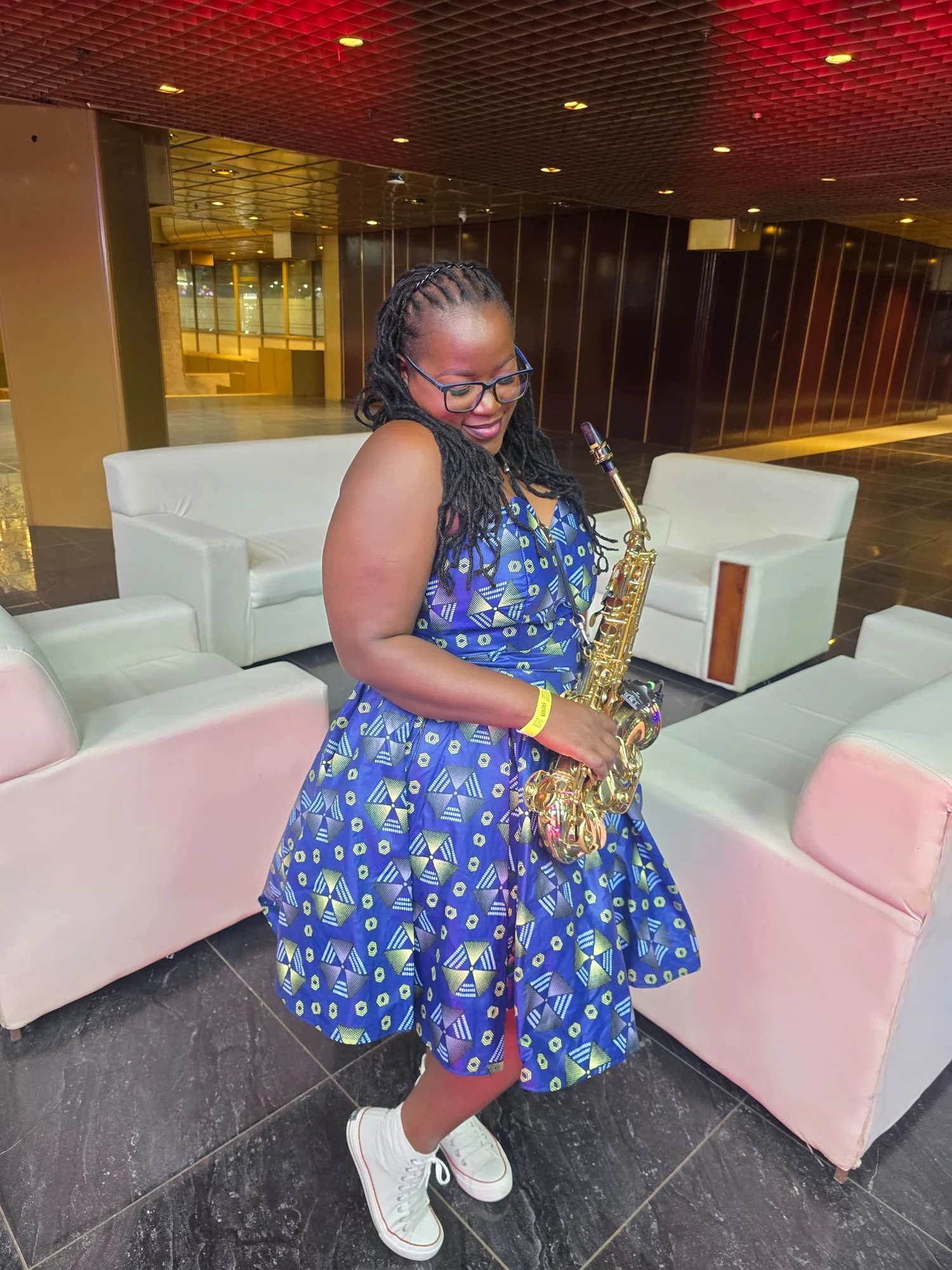 Tina Watyoka with saxophone in a blue patterned dress