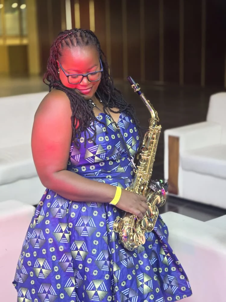 Tina Watyoka with saxophone in a blue patterned dress