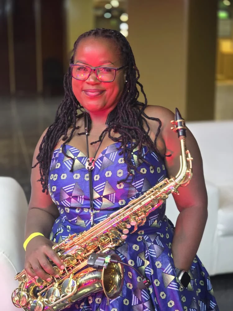 Tina Watyoka with saxophone in a blue patterned dress